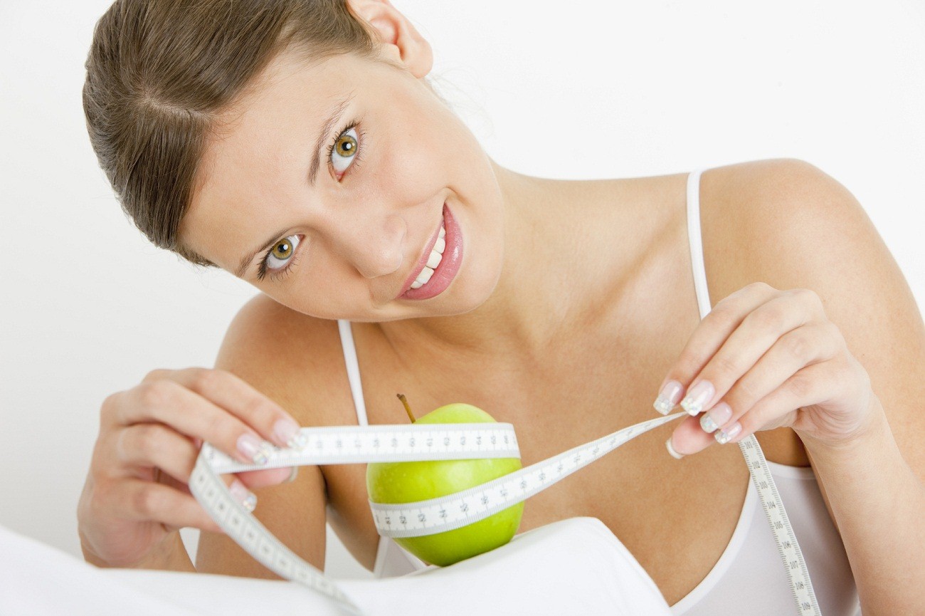 portrait of young woman with green apple and tape measure